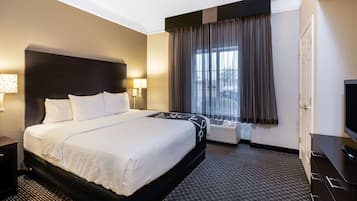 A hotel room with a large bed, a flat-screen TV, a desk, and a window with curtains.