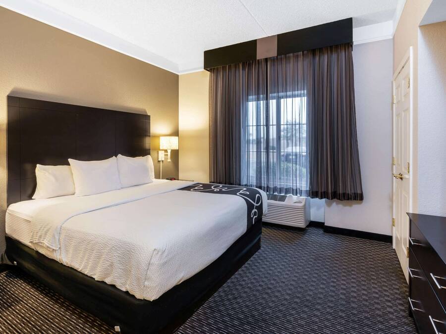 A hotel room with a large bed, a flat-screen TV, a desk, and a window with curtains.
