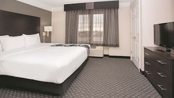 A hotel room with a large bed, a television, a dresser, and a window with curtains.