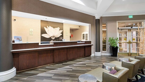 Een hotel receptie met een houten balie, een groot decoratief wandobject en een zithoek met ronde tafels en stoelen.