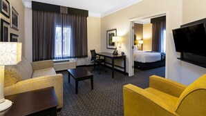 Een hotelkamer met een bank, een kleine tafel, een bureau, een bed, een televisie en een deur naar een andere kamer.