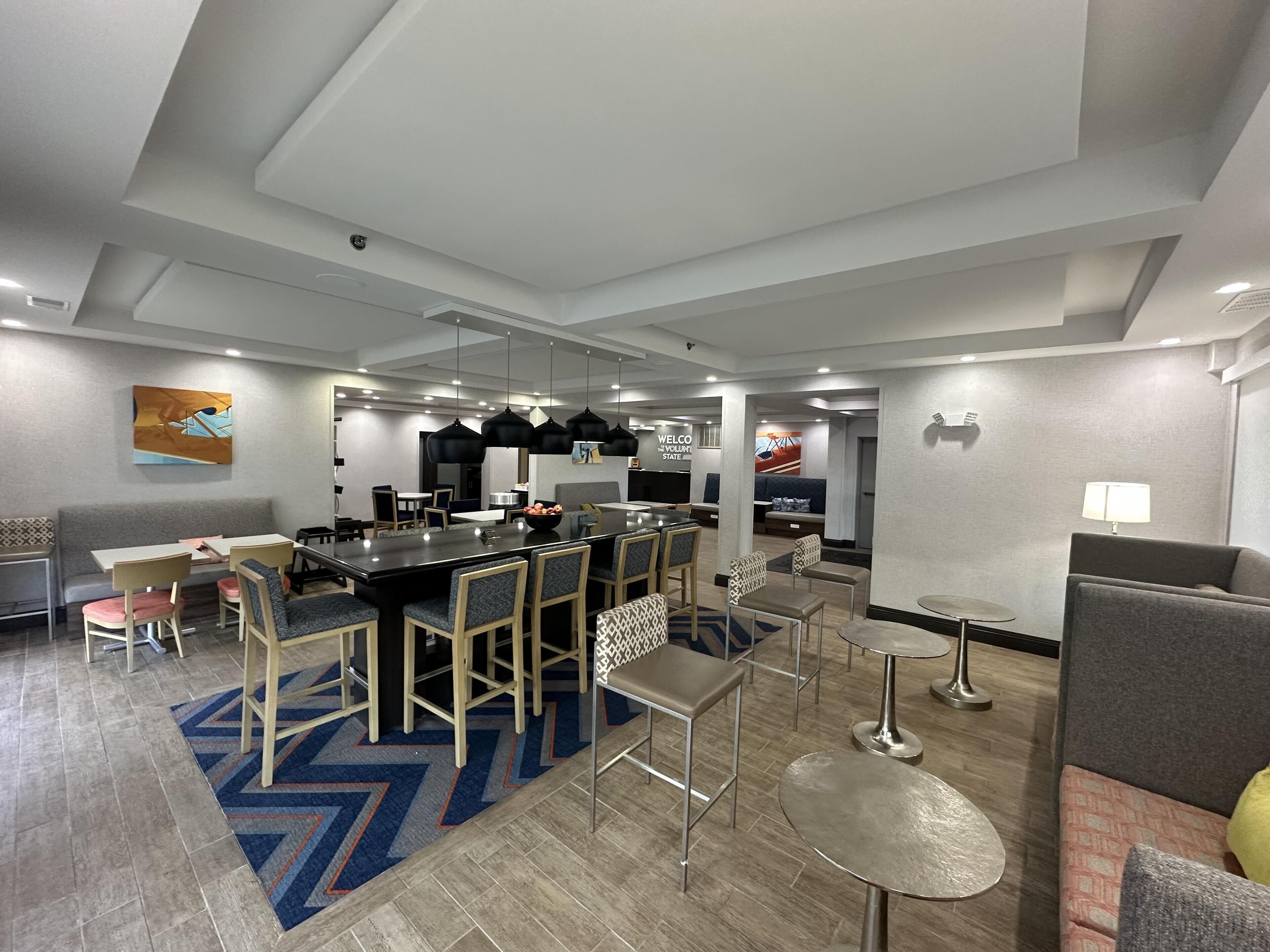 A modern hotel lobby with a central dining area, seating arrangements, and a reception desk.