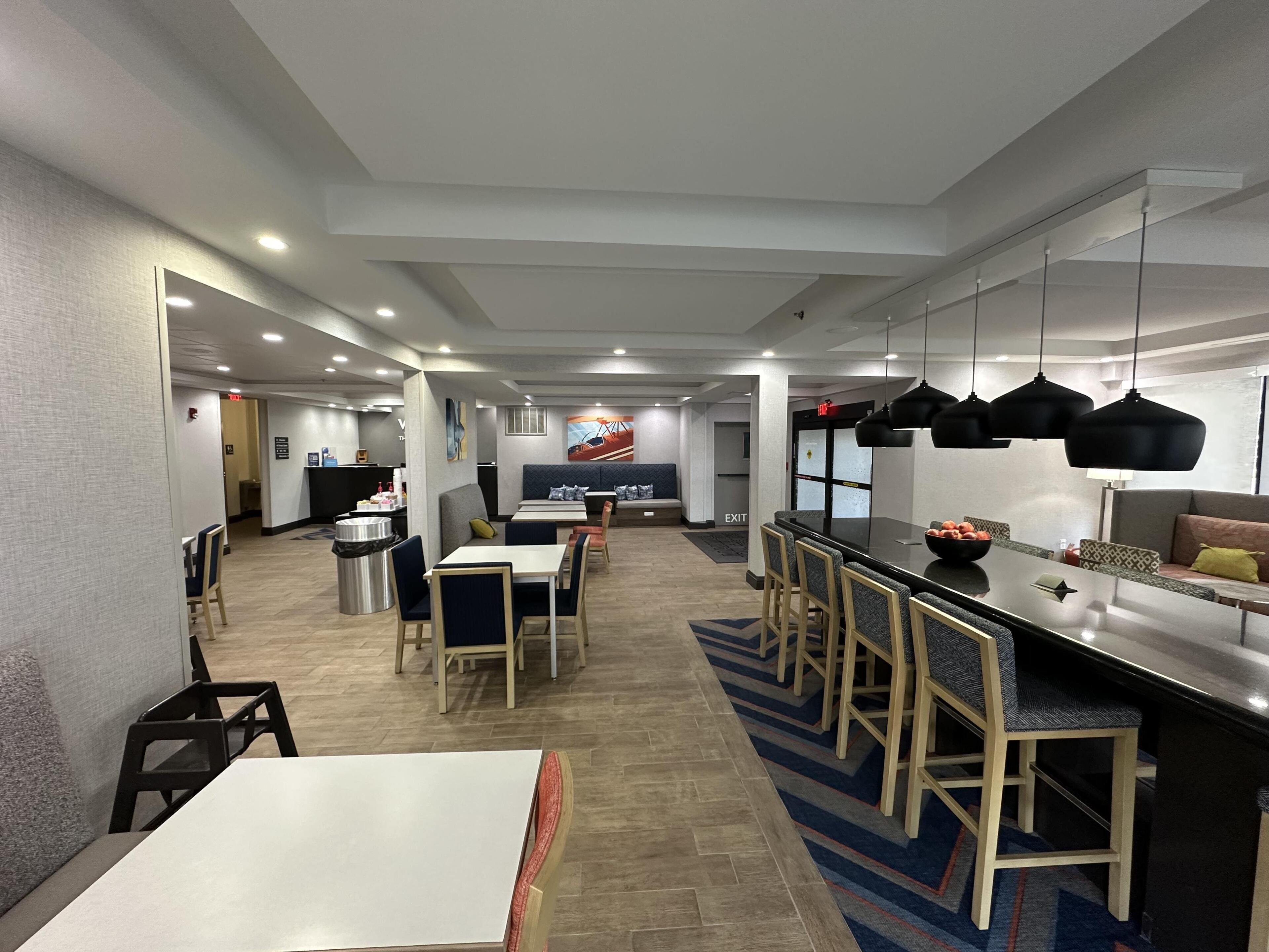Una hall moderna di un hotel con un'area bar, posti a sedere e un cartello di uscita ben visibile.