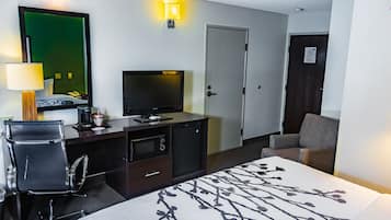 A hotel room with a bed, desk, chair, television, and a door.