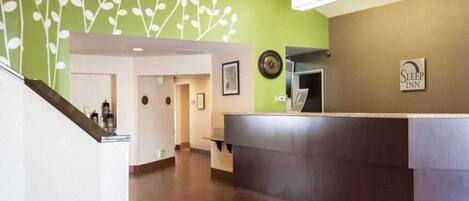 Zona de recepción de un hotel con una pared verde, mostrador de recepción y una escalera.