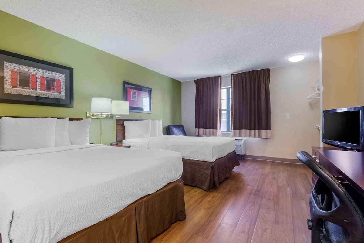 A hotel room with two beds, a TV, a desk, and a window with curtains.