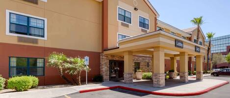 A hotel with a beige facade, a covered lobby area, and a parking lot with handicapped parking.