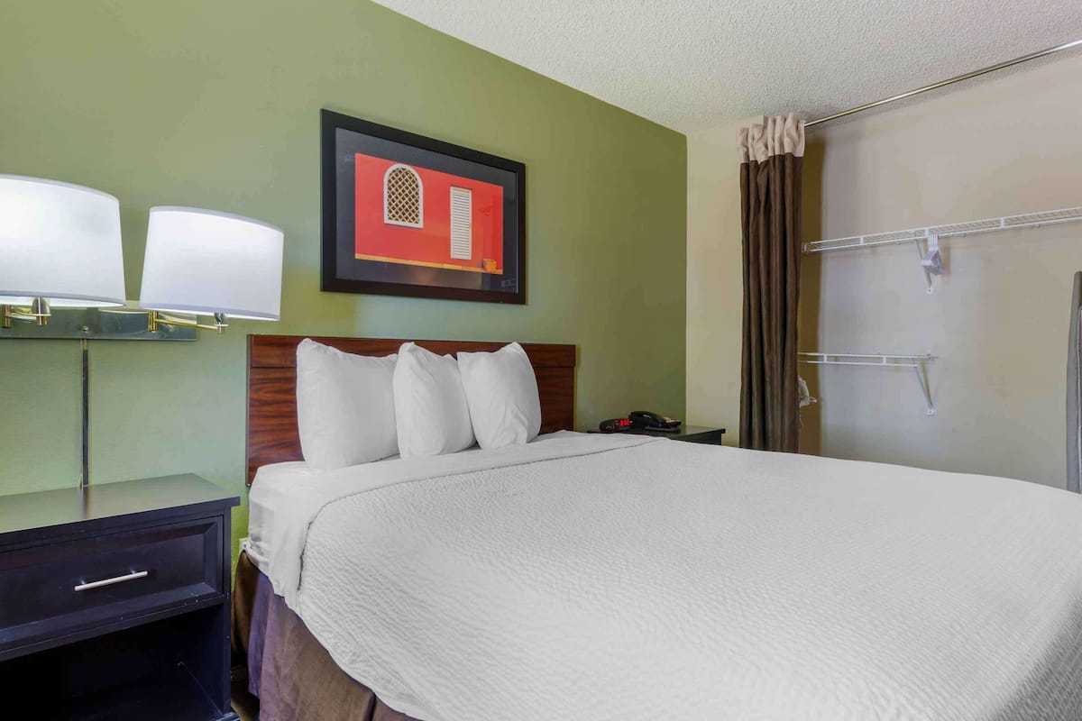 A hotel room with a bed, a nightstand with lamps, a framed picture on the wall, and a shower area.