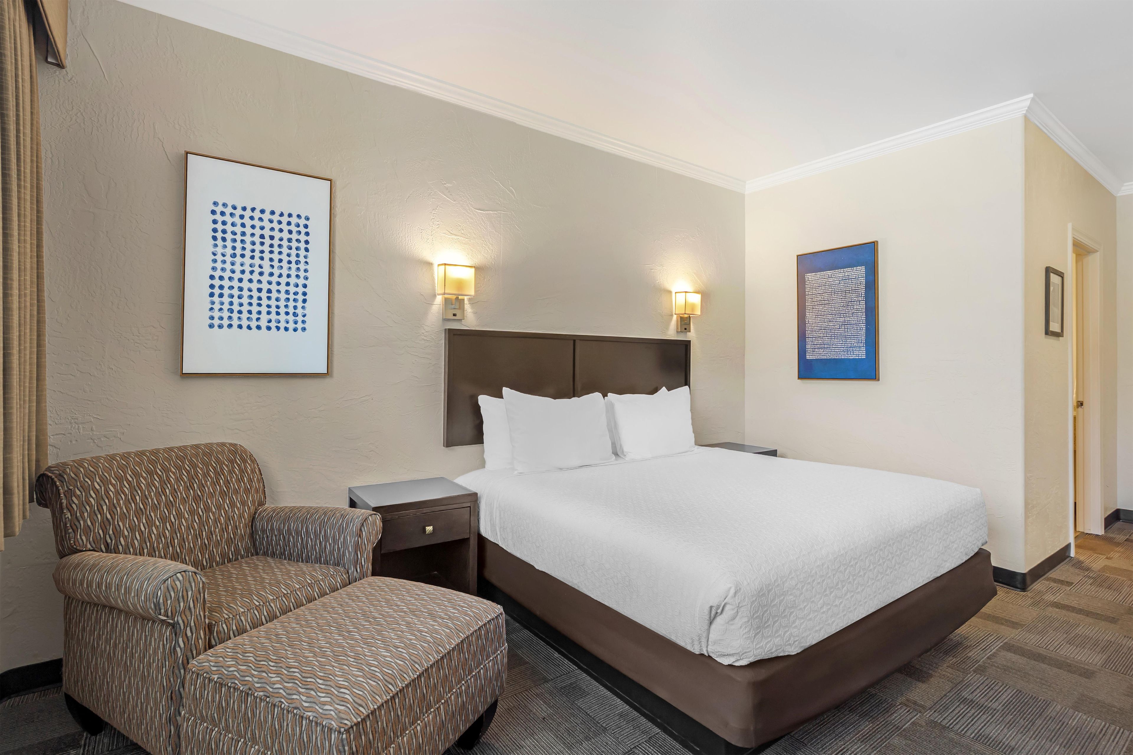 A hotel room with a bed, a chair, a nightstand, and two wall-mounted lamps.