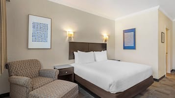 A hotel room with a bed, a chair, a nightstand, and two wall-mounted lamps.
