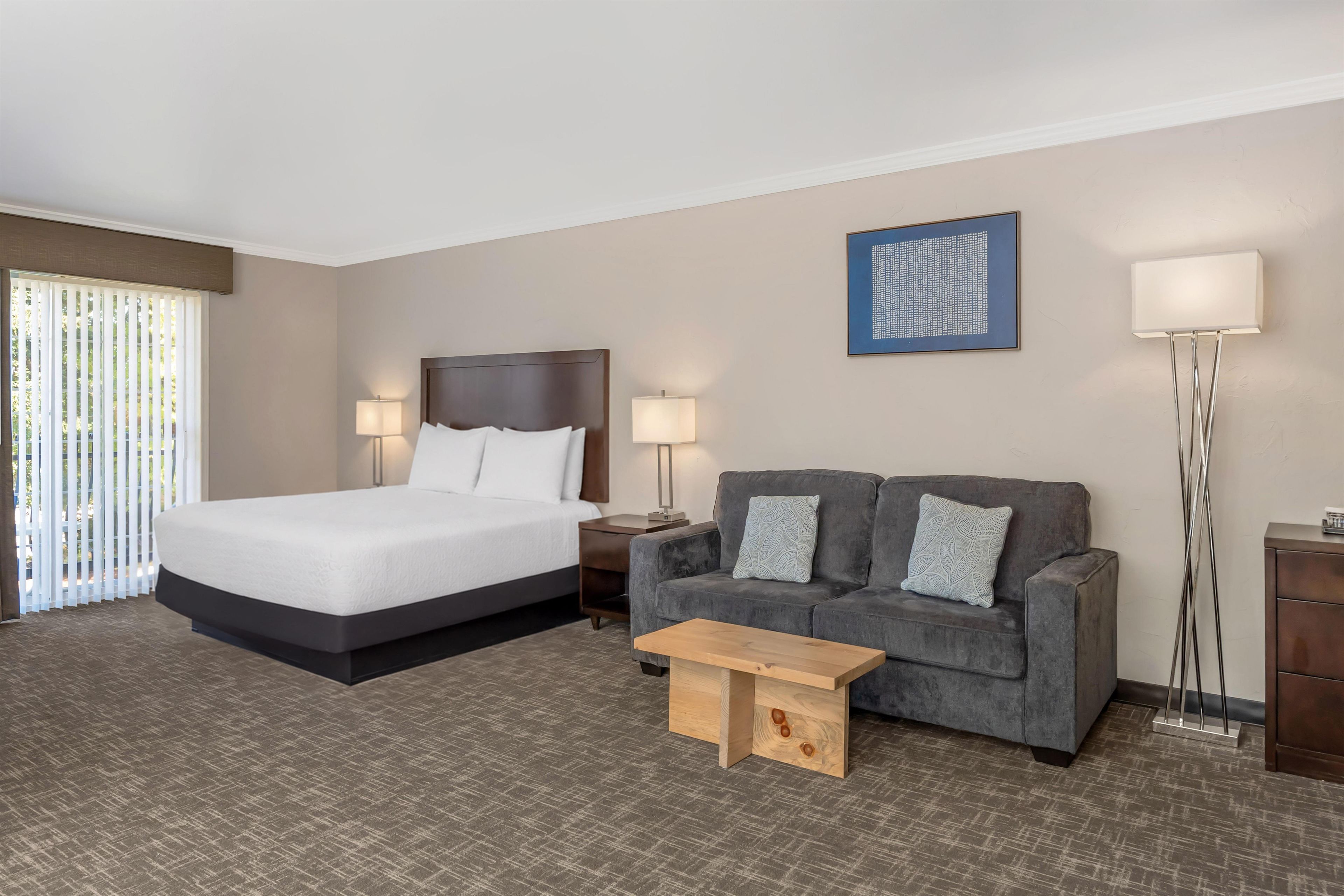 Habitación de hotel con cama, sofá, mesa de centro, lámpara de pie y un cuadro en la pared.
