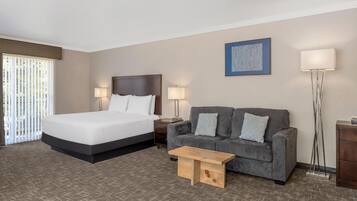 Habitación de hotel con cama, sofá, mesa de centro, lámpara de pie y un cuadro en la pared.