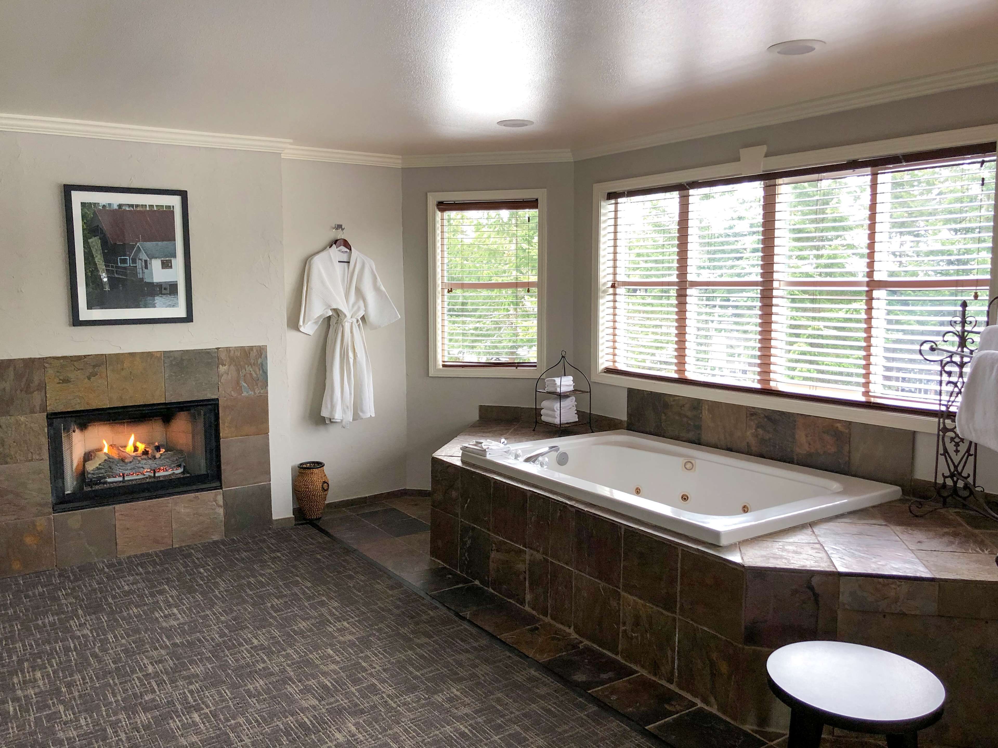 A bathroom with a fireplace, a large bathtub, and a window with blinds.