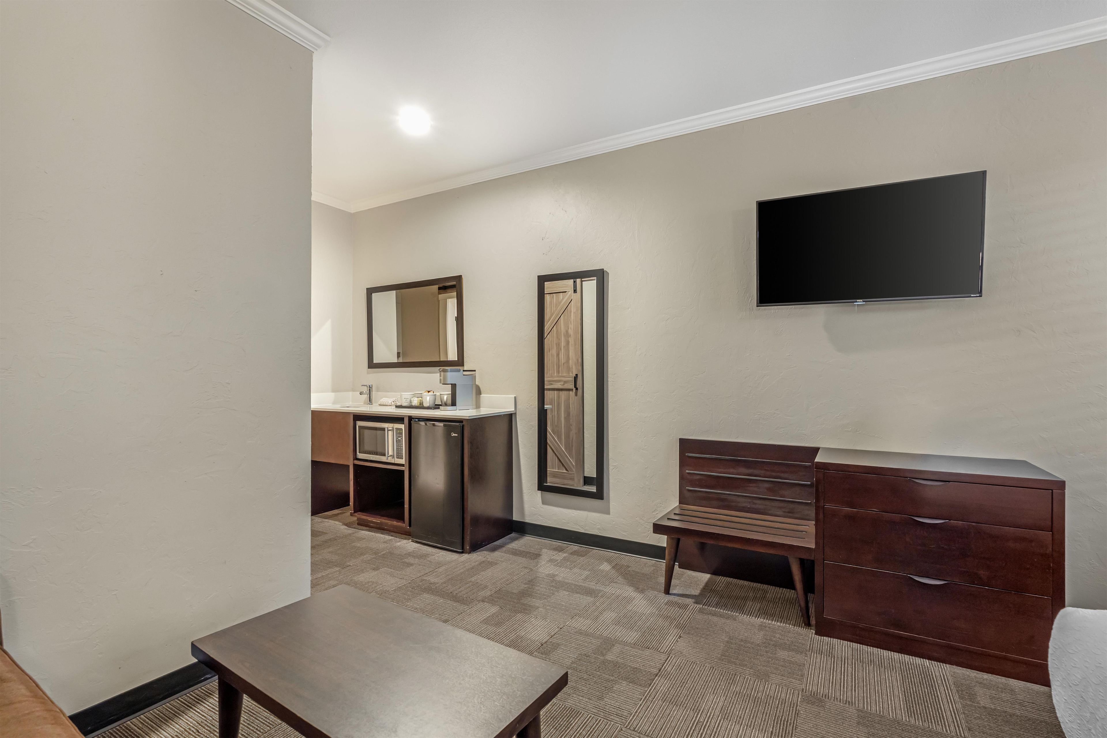 A hotel room with a flat-screen TV, a wooden dresser, a bench, a microwave, and a large mirror.