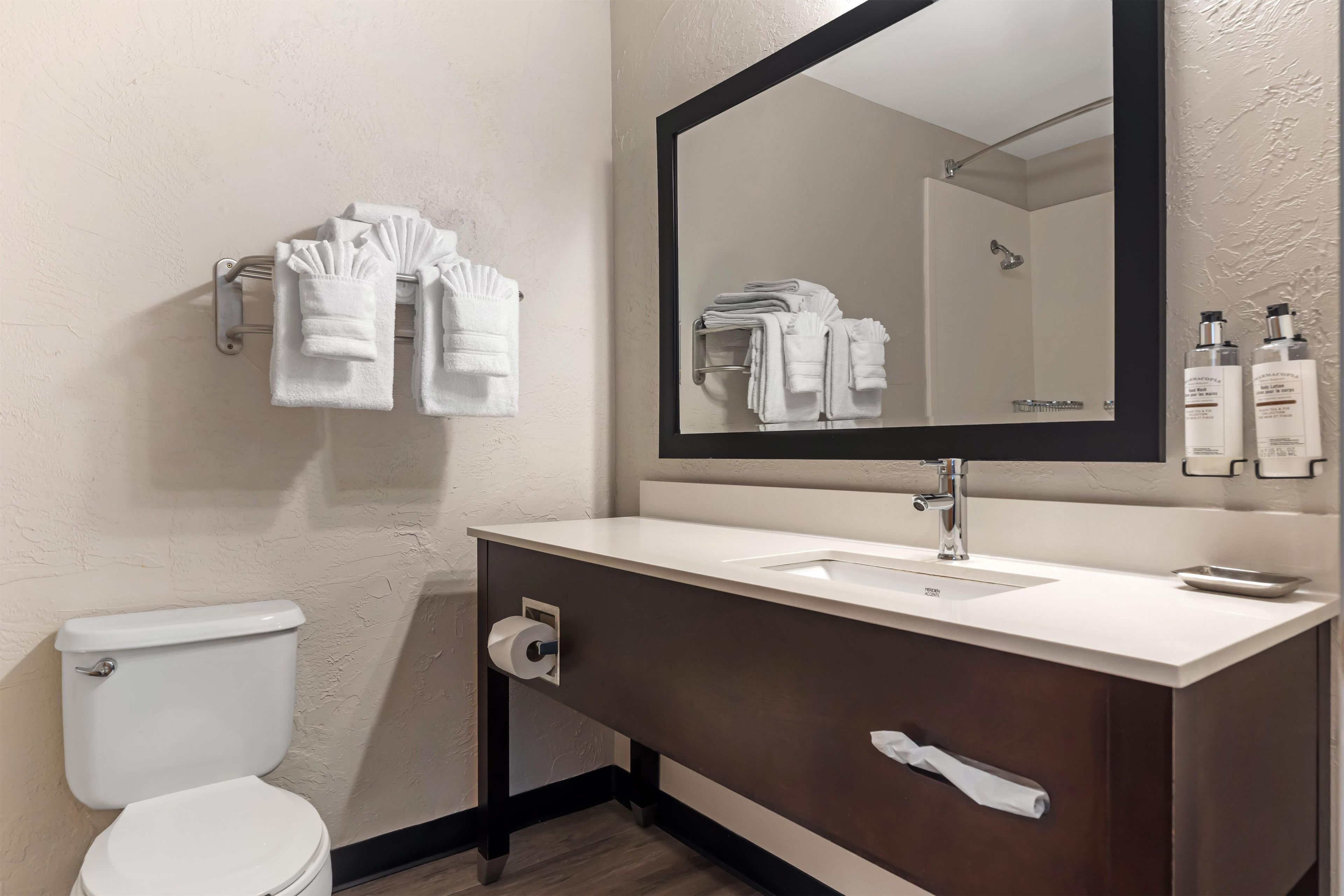 A bathroom with a white toilet, a sink, a mirror, and towels on a towel rack.