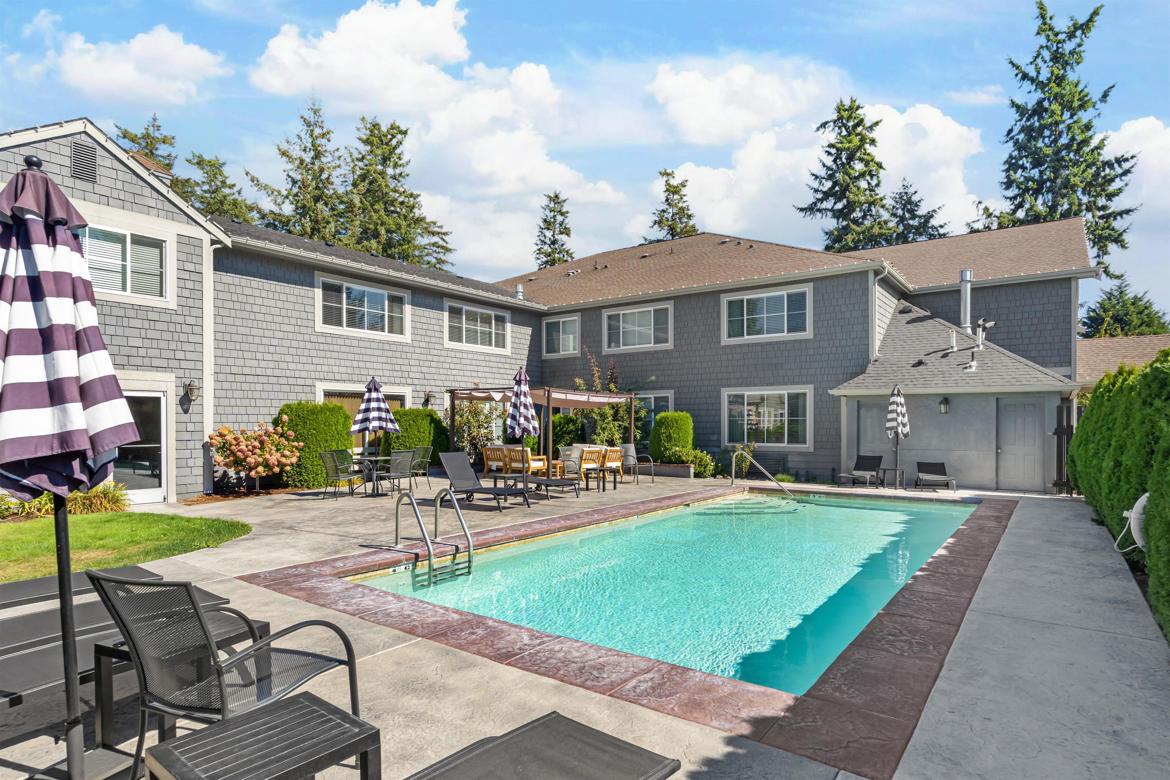 A residential swimming pool with a patio area, lounge chairs, and a covered seating area.