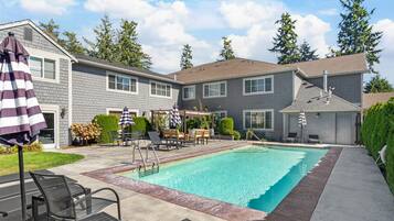 A residential swimming pool with a patio area, lounge chairs, and a covered seating area.