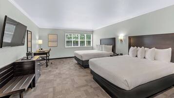 A hotel room with two beds, a desk, a chair, a TV, and a window.
