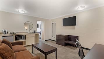 A modern living room with a brown sofa, a coffee machine, a microwave, a flat-screen TV, and a desk with drawers.