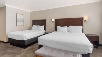 A hotel room with two beds, a bench, and a framed picture on the wall.