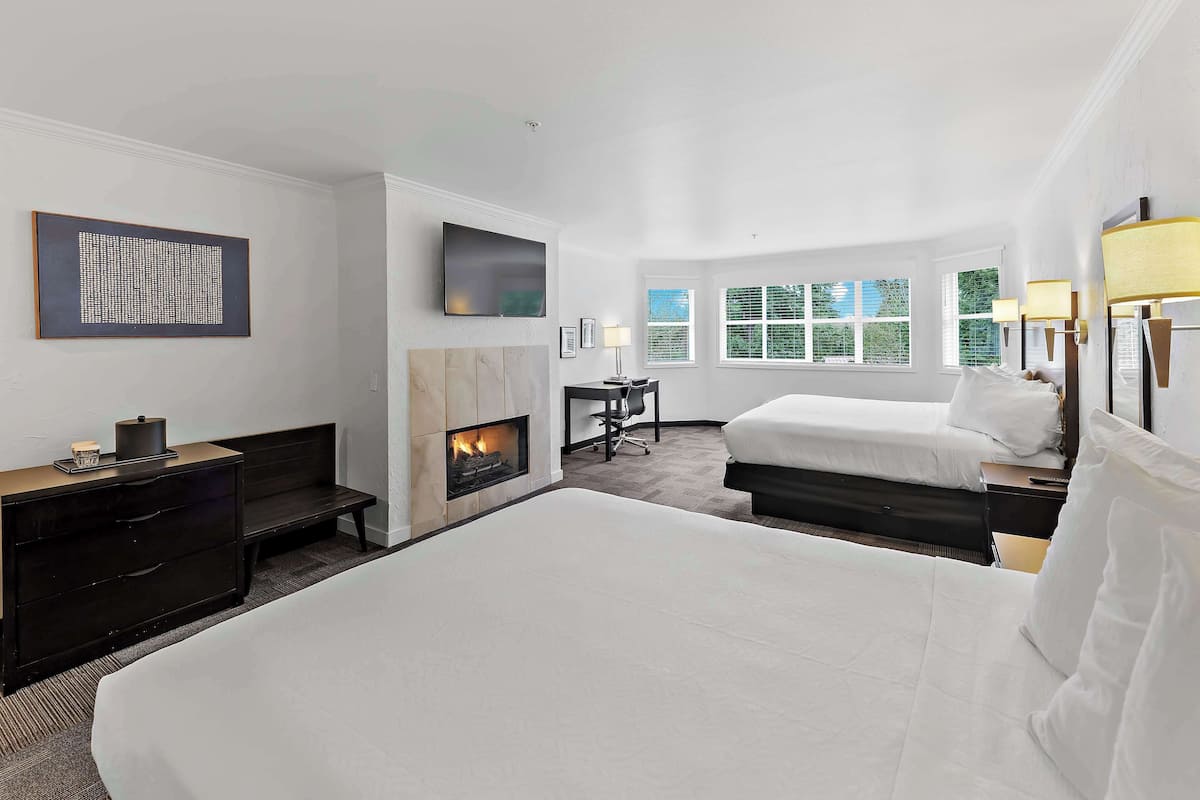 Quarto de hotel com uma cama grande, uma escrivaninha com cadeira, lareira e várias janelas.