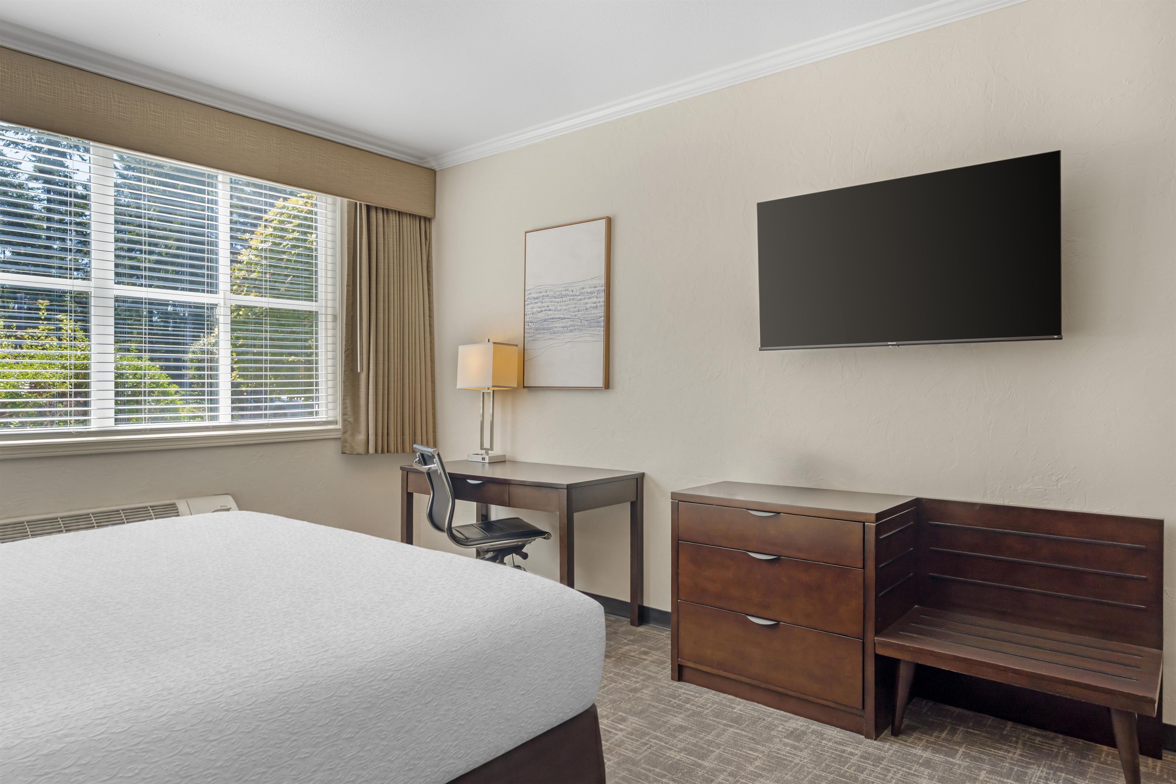 Habitación de hotel con cama, escritorio, silla y televisor de pantalla plana montado en la pared.