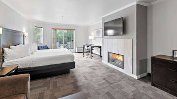 A modern hotel room with a bed, desk, chair, fireplace, and a TV mounted on the wall.