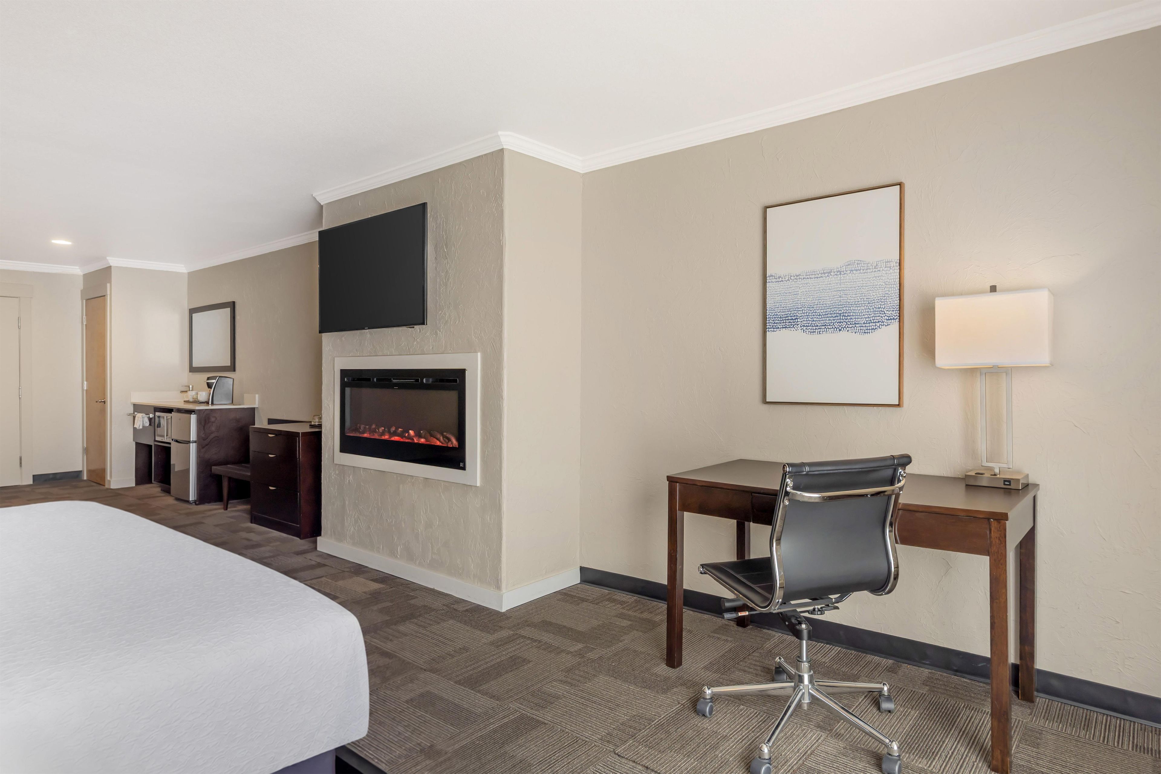 A hotel room with a bed, a desk, a chair, a fireplace, a television, and a framed picture on the wall.
