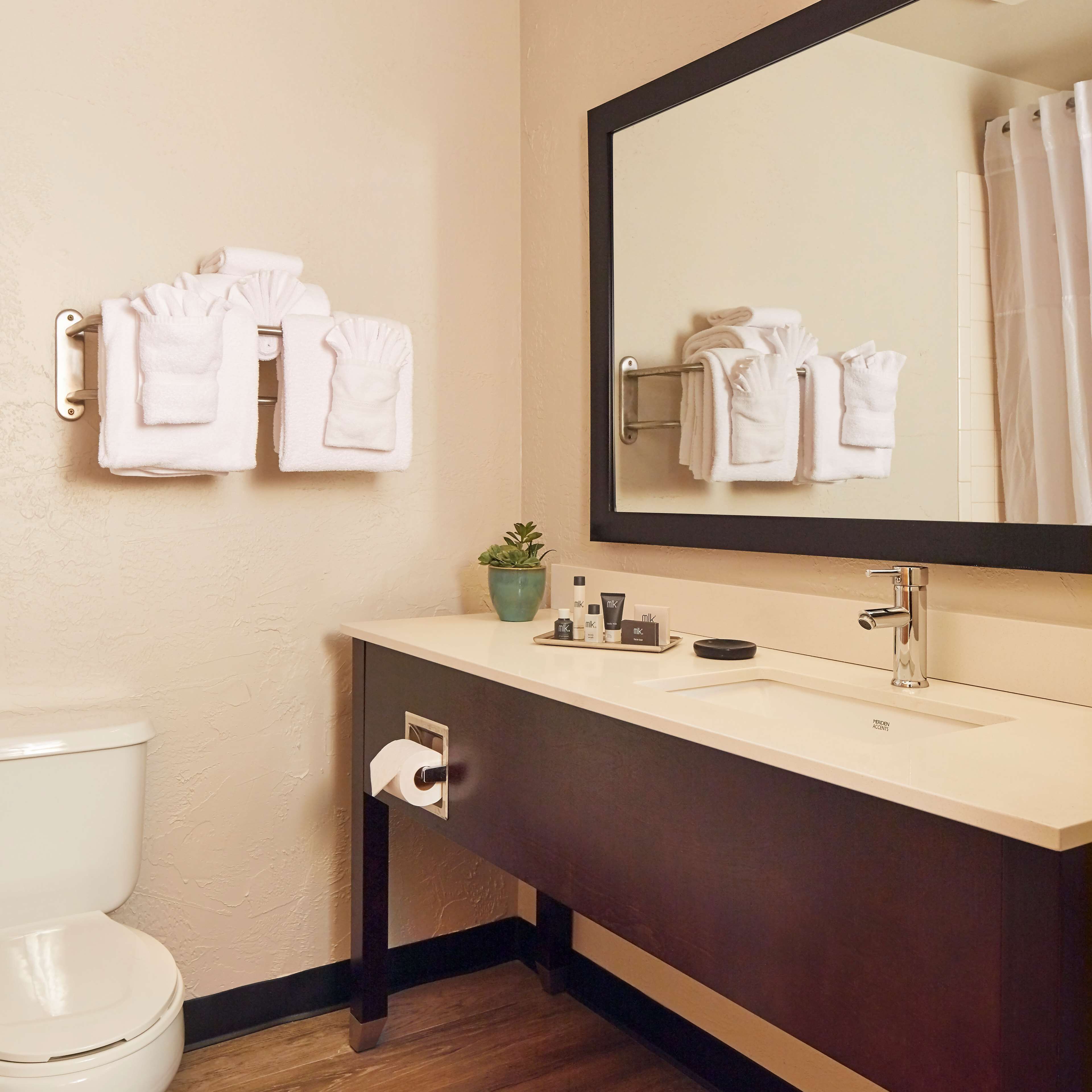A bathroom with a toilet, a sink with toiletries, and towels hanging on a rack.