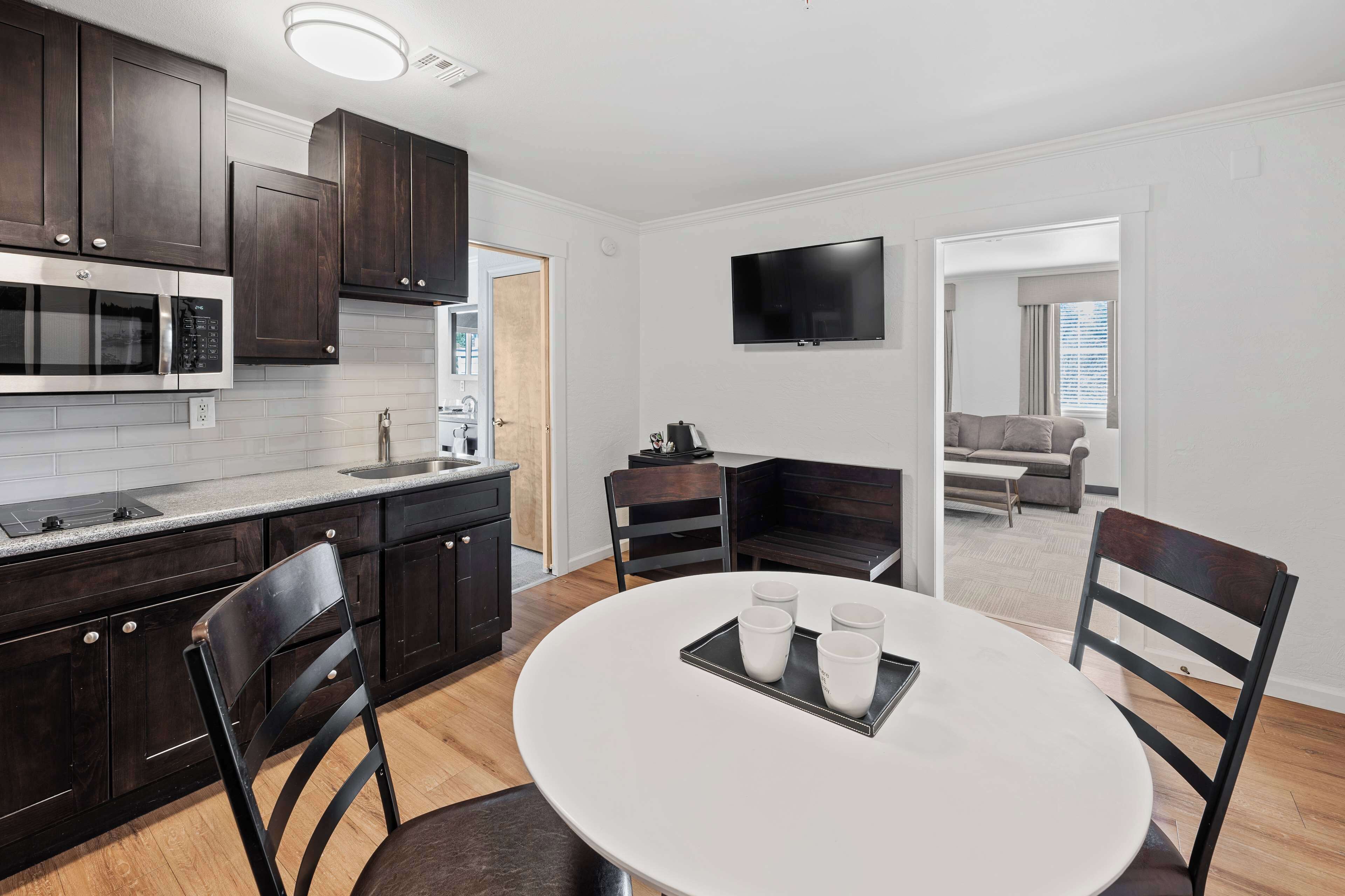 A modern kitchen with dark wood cabinets, a built-in microwave, and a dining area with a white table and chairs.