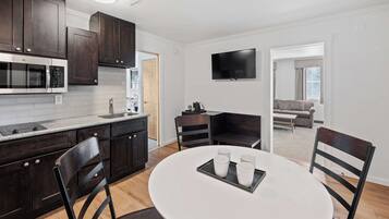 A modern kitchen with dark wood cabinets, a built-in microwave, and a dining area with a white table and chairs.