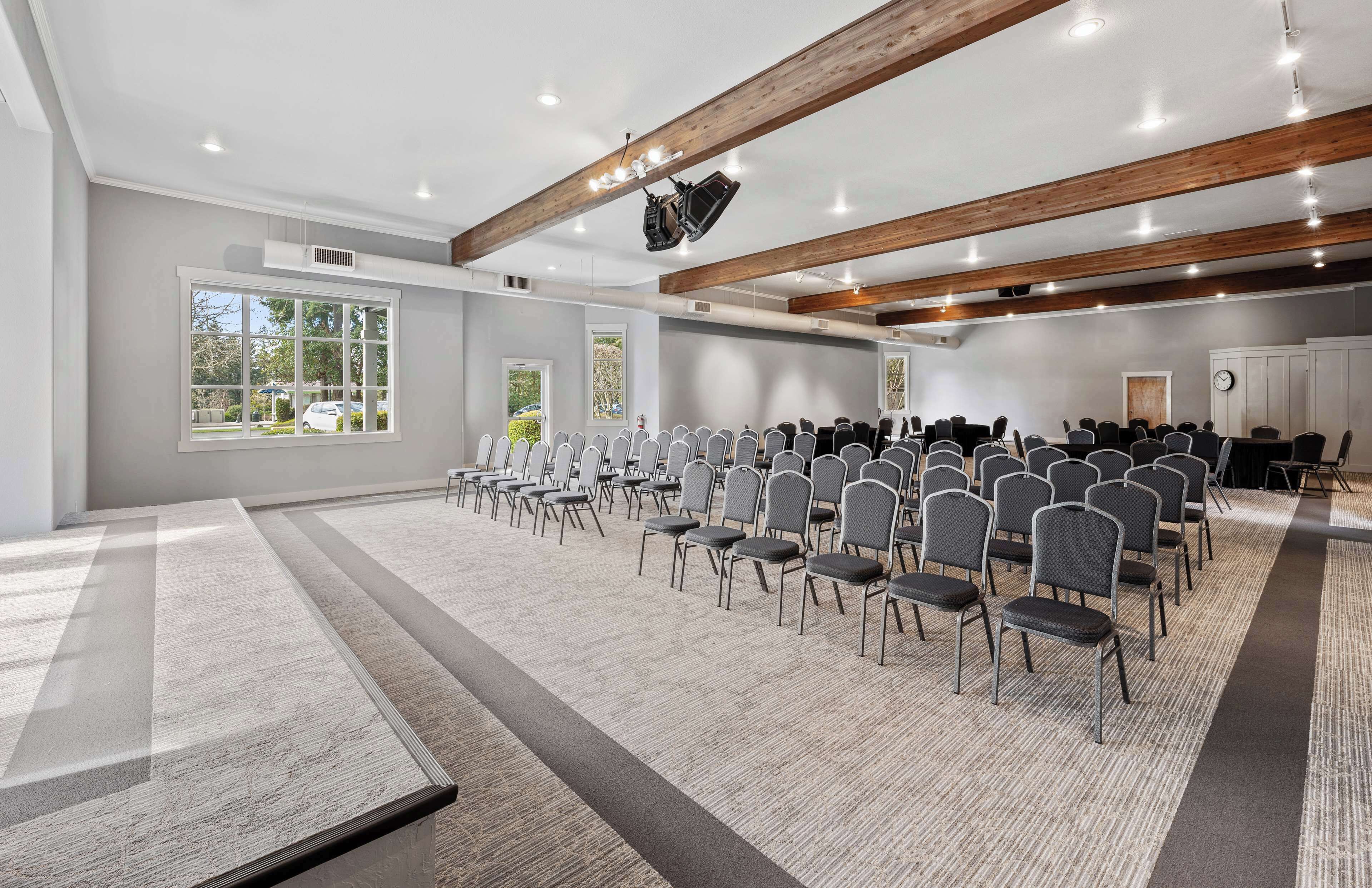 A conference room with rows of chairs, large windows, wooden beams, and ceiling lights.