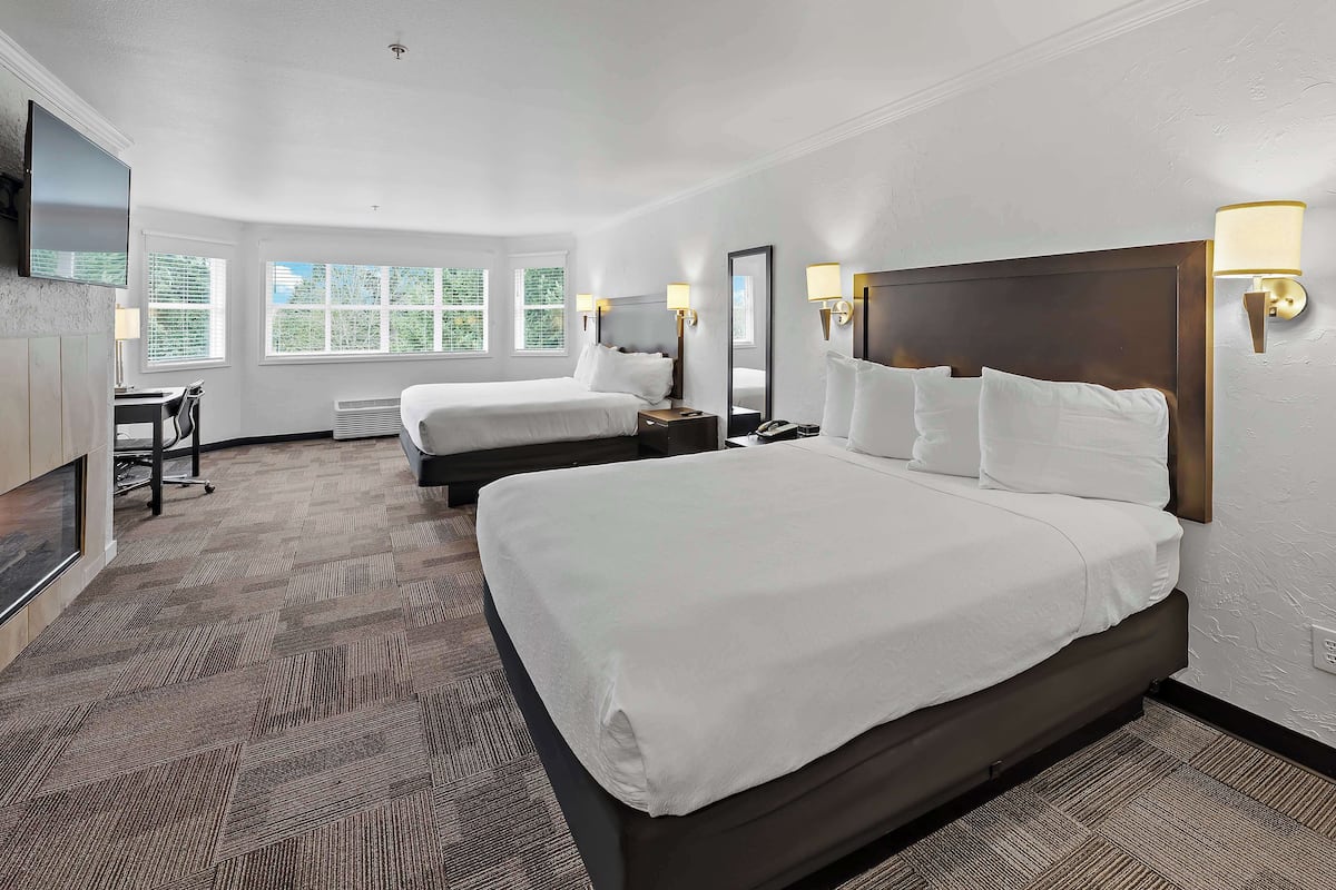 Quarto de hotel com duas camas, uma escrivaninha, uma cadeira, uma televisão e uma janela com persianas.