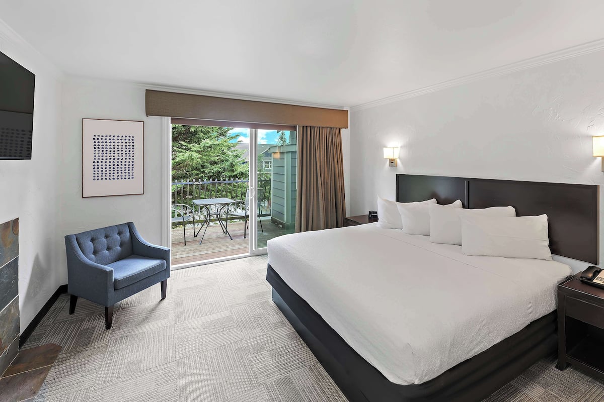 Quarto de hotel com uma cama grande, uma cadeira, uma mesa de cabeceira e vista para o exterior.