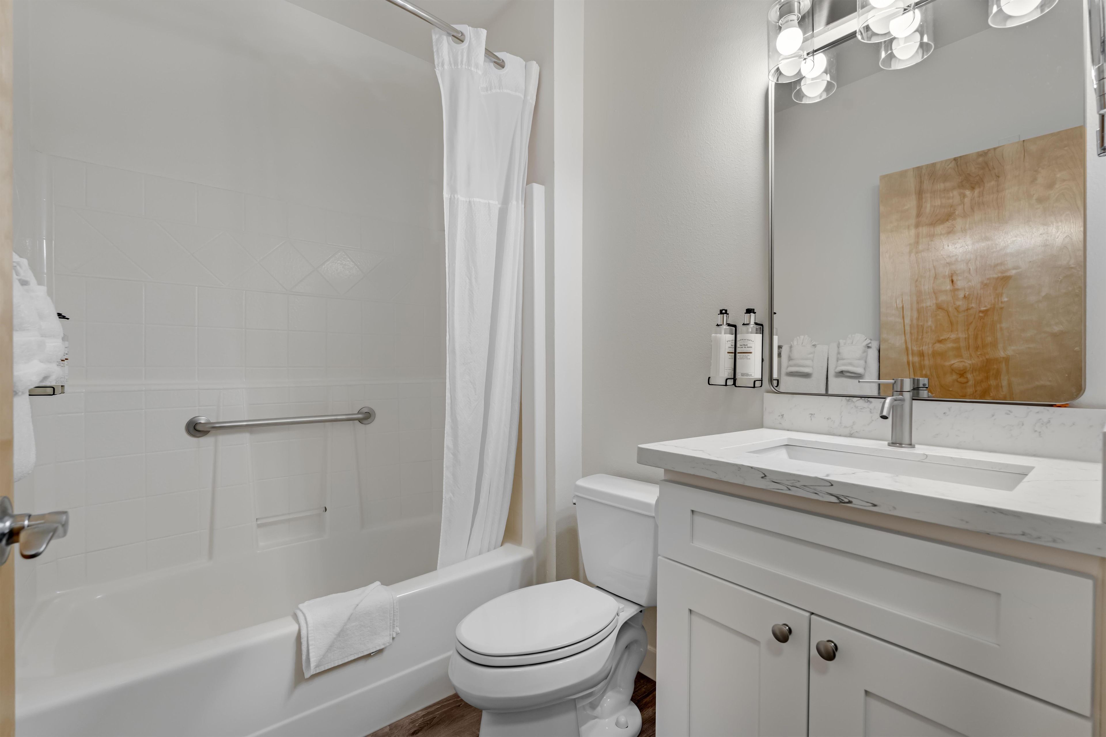 A bathroom with a bathtub, toilet, vanity with a mirror, and a shower curtain.