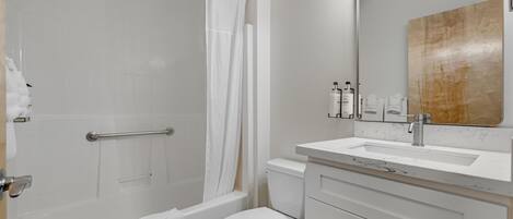 A bathroom with a bathtub, toilet, vanity with a mirror, and a shower curtain.