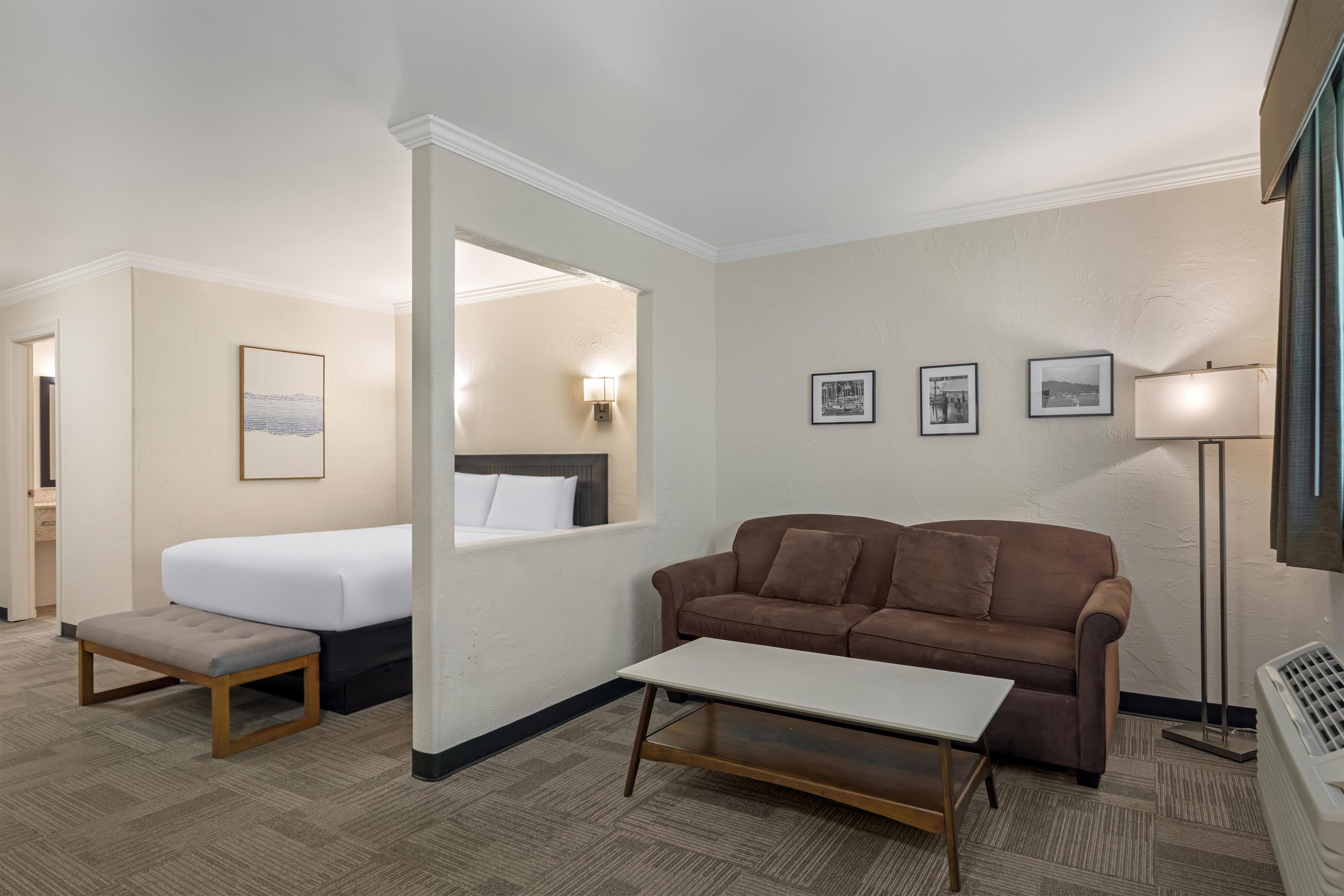 Ein Hotelzimmer mit einem Bett, einer Couch, einem kleinen Tisch und einem Spiegel. An den Wänden sind Wandleuchten und gerahmte Bilder angebracht.