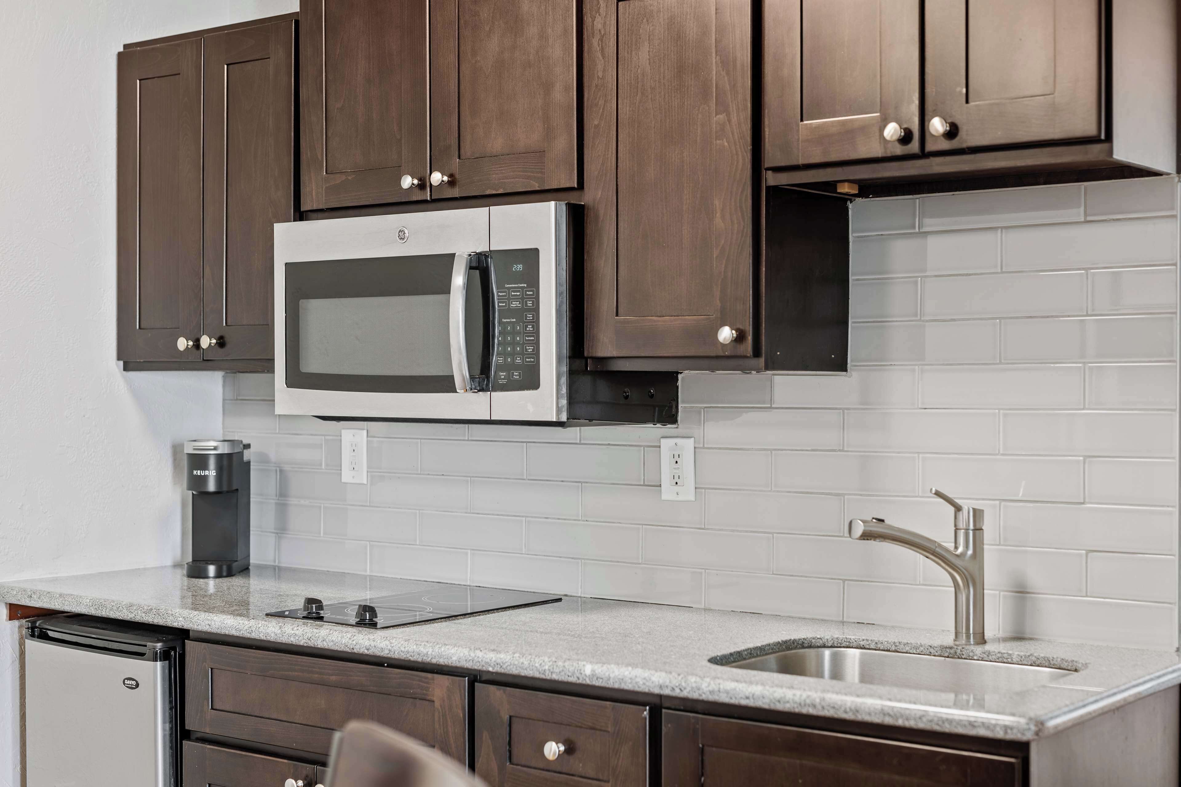 A kitchen with dark wooden cabinets, a stainless steel microwave, a coffee maker, and a sink with a modern faucet.