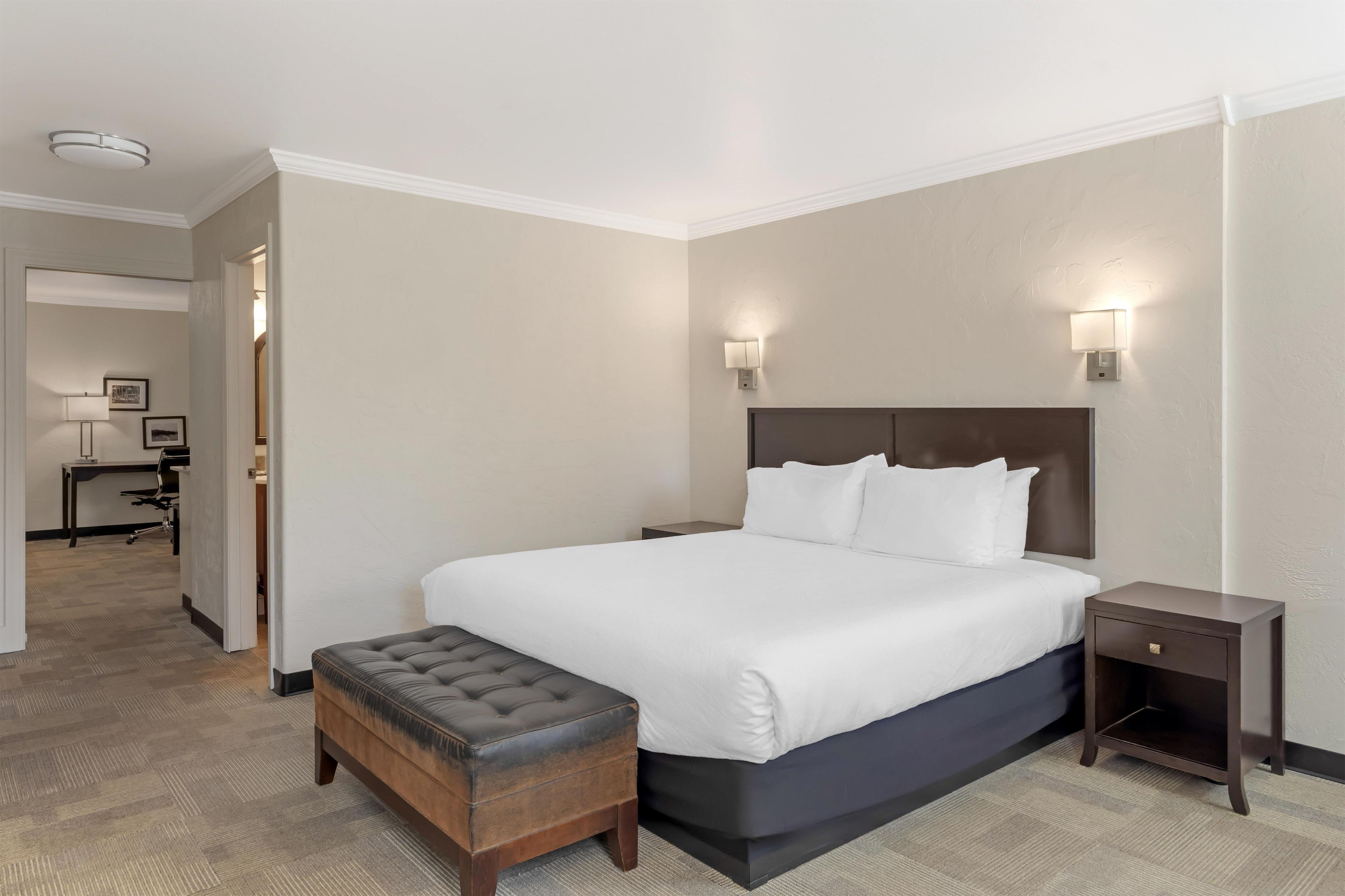 A hotel room with a large bed, a bedside table, a nightstand, a lamp, and a chair.
