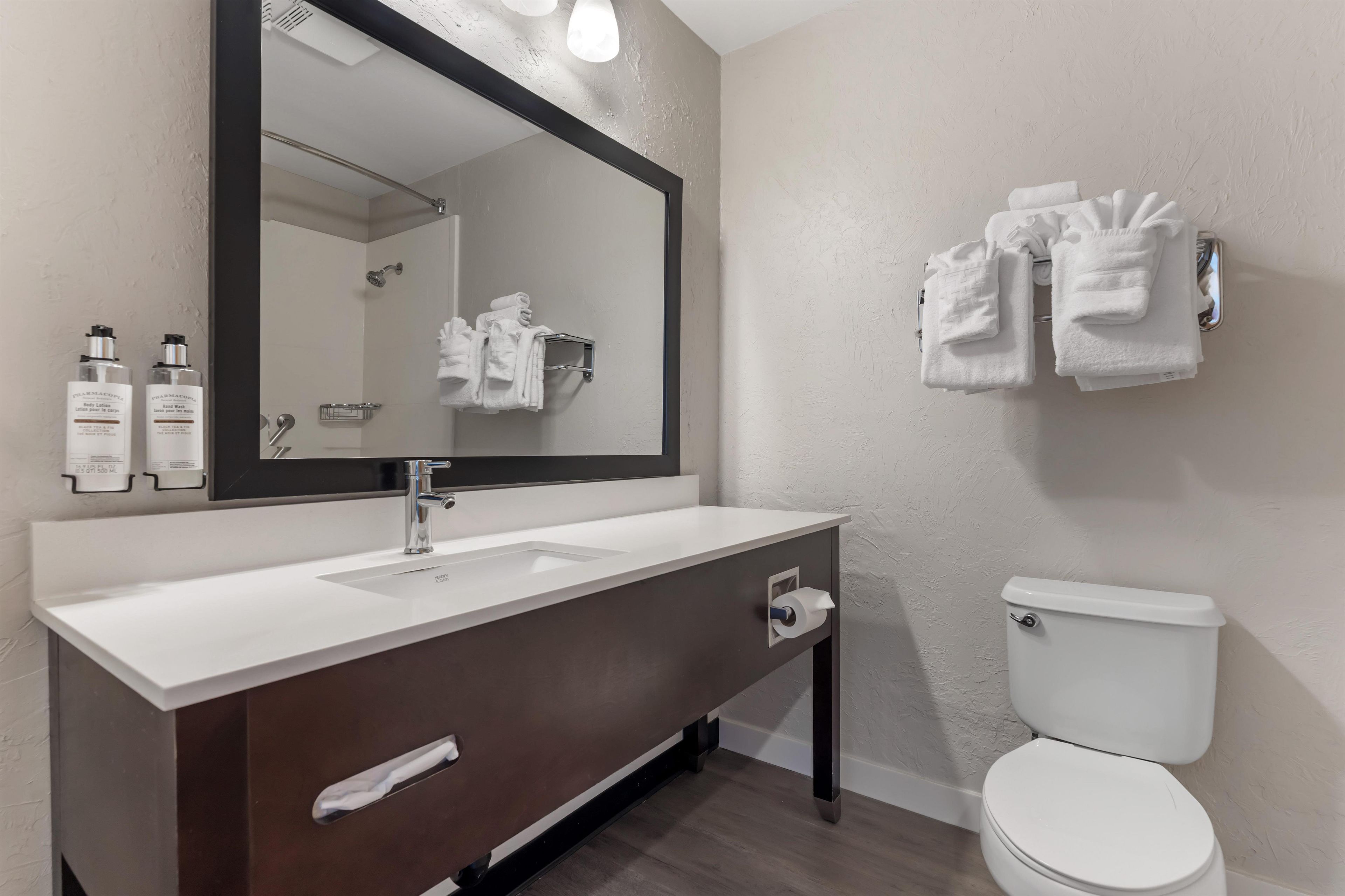 A modern bathroom with a white sink, dark wooden vanity, a large mirror, and a white toilet.