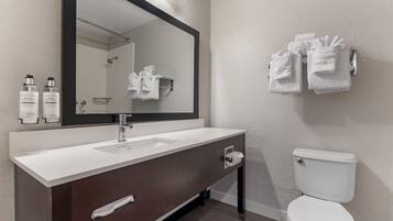 A modern bathroom with a white sink, dark wooden vanity, a large mirror, and a white toilet.