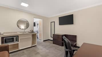 A hotel room with a kitchenette, a flat-screen TV, a mirror, and a desk with a chair.