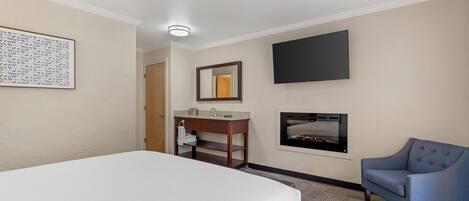 A hotel room with a bed, a desk with a mirror, a flat-screen TV, and a fireplace.