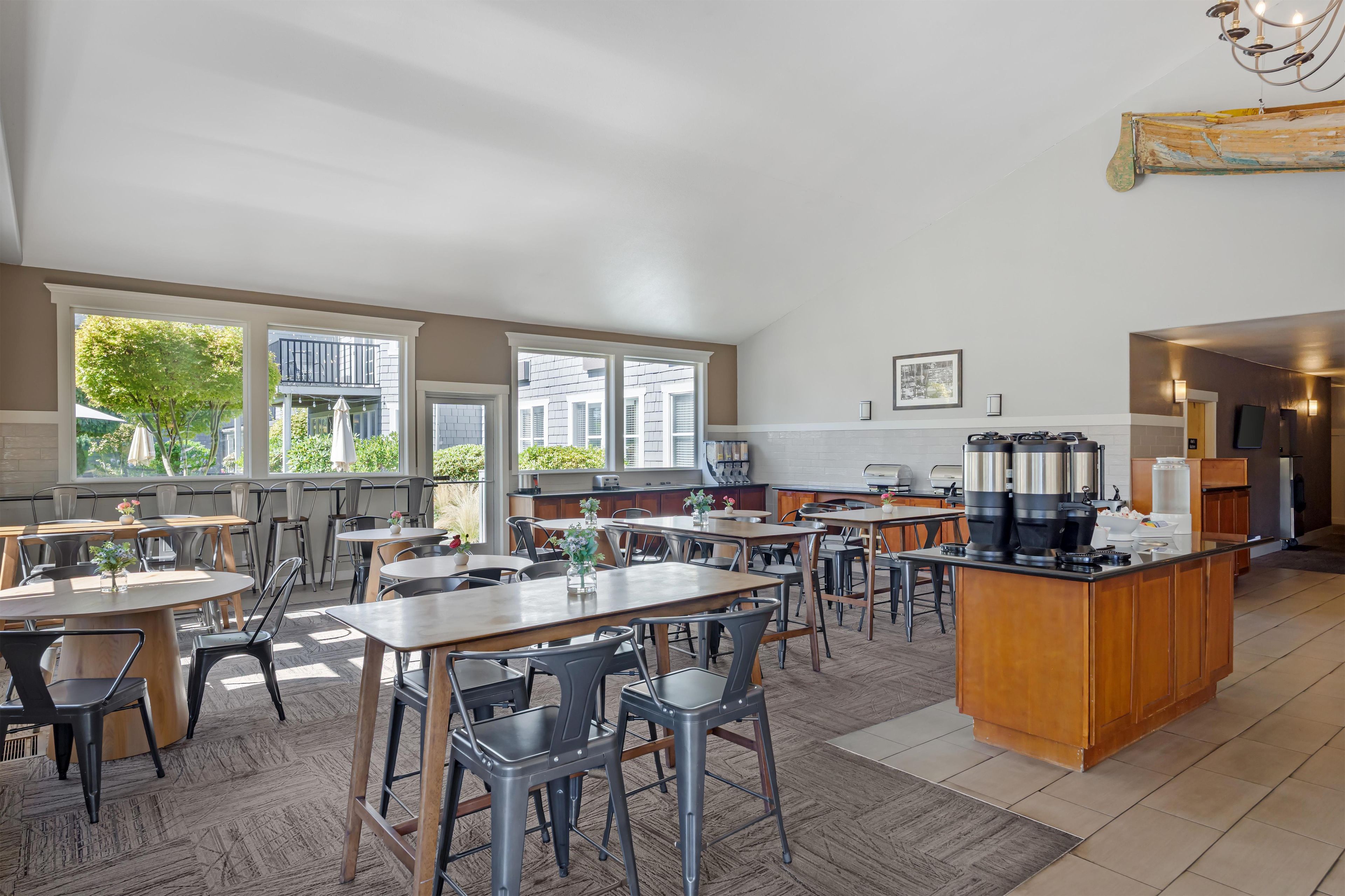 A spacious dining area with multiple tables and chairs, large windows, and a kitchen area with modern appliances.