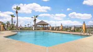 A rectangular swimming pool with a thatched-roof pavilion, palm trees, and lounge chairs.