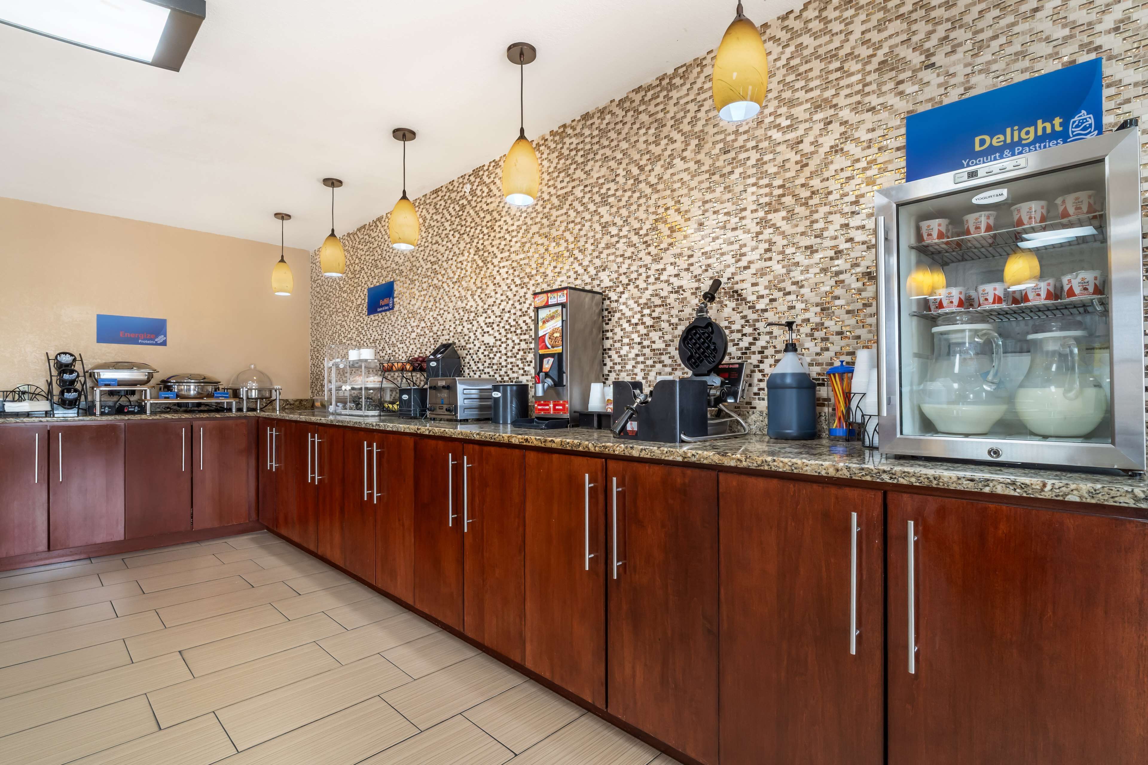 Un bar à petit-déjeuner avec un présentoir de yaourts et de viennoiseries, une machine à gaufres et un espace dédié au café.