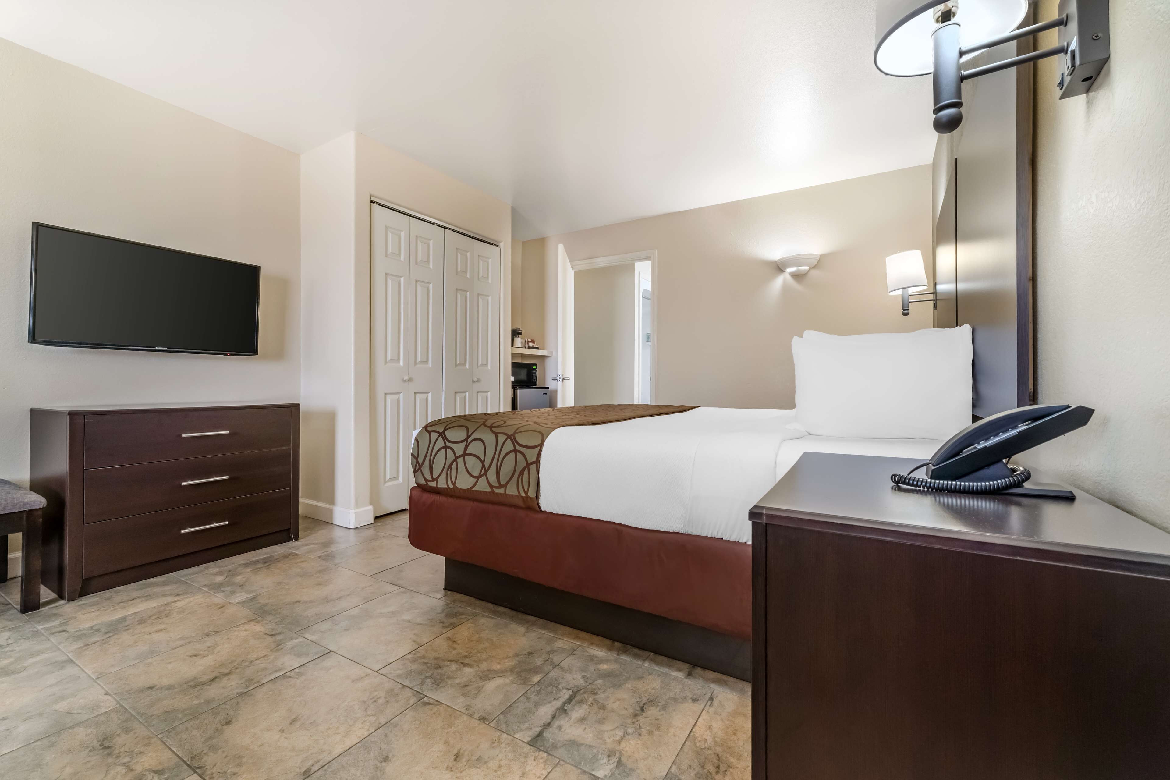 Una habitación de hotel con cama, escritorio con teléfono, televisión y armario.