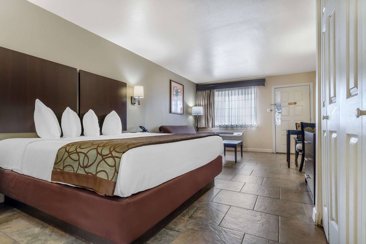 A hotel room with a large bed, a desk, a chair, and a window with curtains.