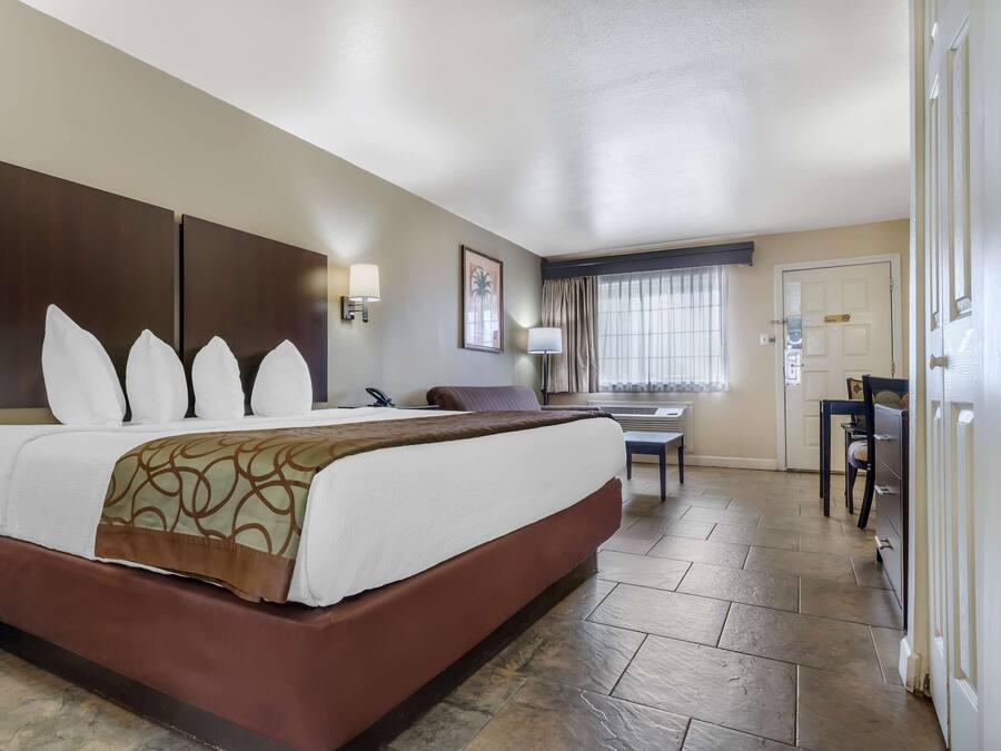Una habitación de hotel con una cama grande, un escritorio, una silla y un ventanal con cortinas.
