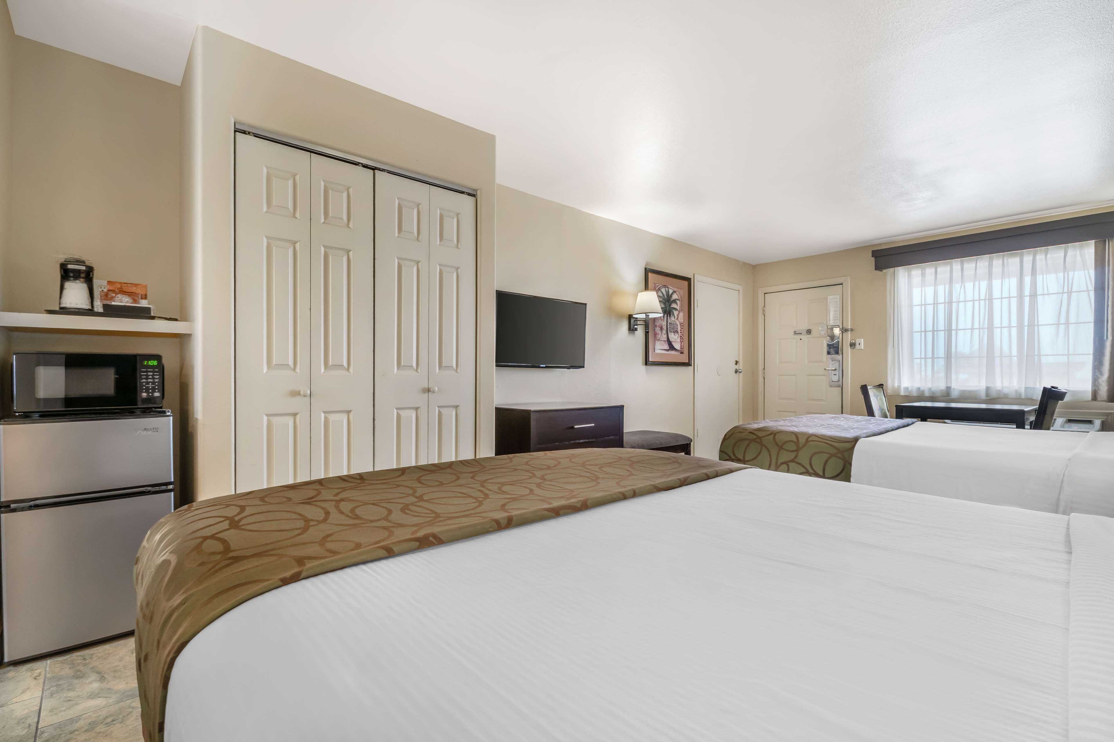 A hotel room with a bed, a microwave, a refrigerator, a television, and a window with curtains.